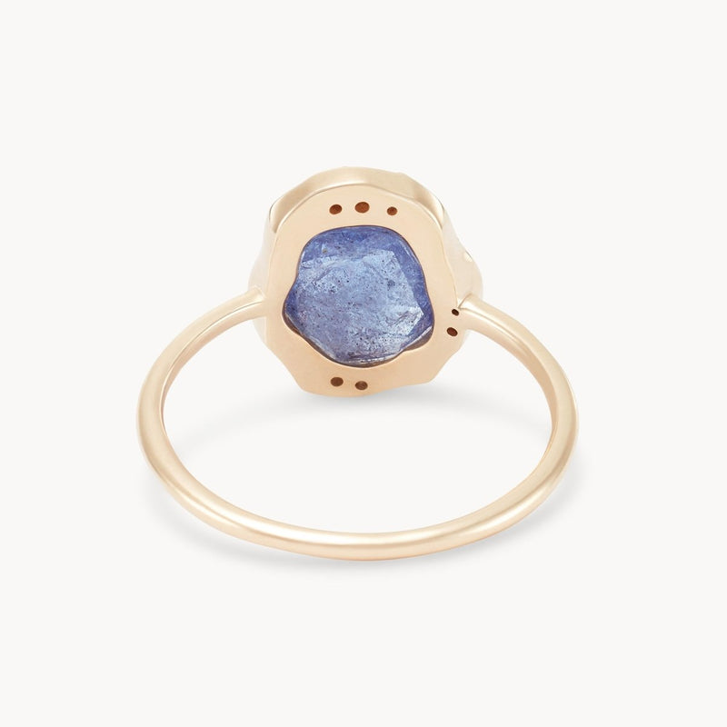 The tanzanite mood ring by bluboho features a roughly cut, irregularly shaped blue tanzanite gemstone mounted at its center. This 14k yellow gold ring boasts a minimalist design with a thin, smooth band and a unique setting that showcases the natural beauty of the gemstone.