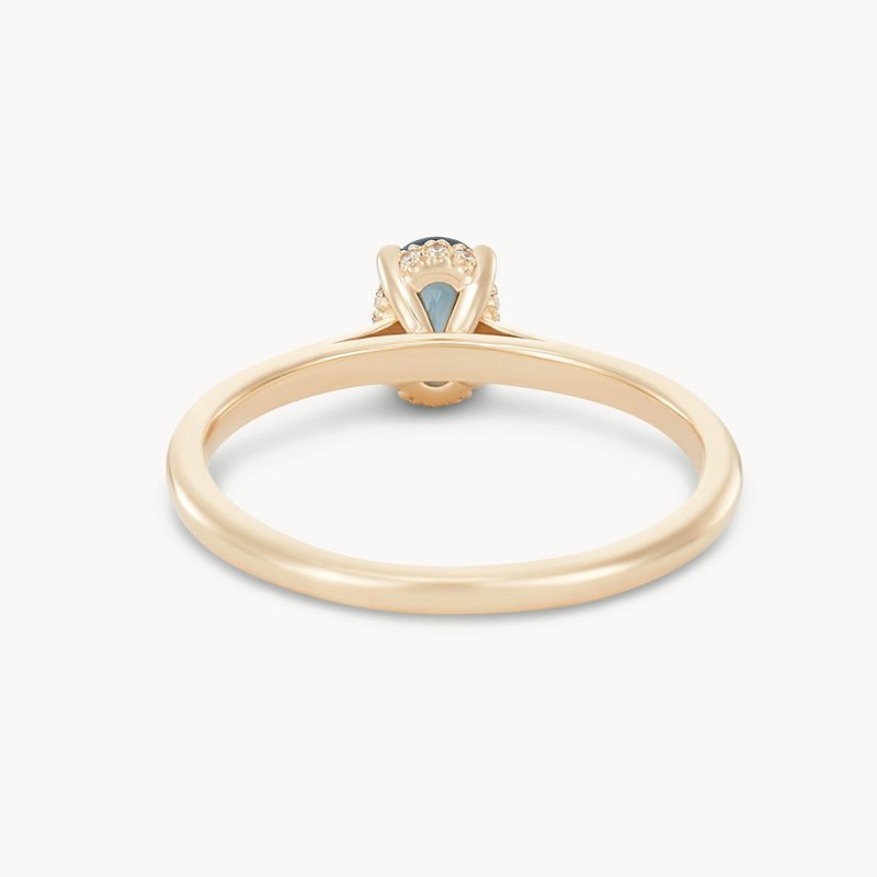 An elegant 14k yellow gold engagement ring, featuring a single raised, round blue sapphire in a prong setting. Crafted by beloved by bluboho under the name "astral love one-of-a-kind," it boasts a smooth and plain band leading up to an intricate setting that elevates the sapphire as the focal point. The backdrop is plain white, which accentuates the exquisite design of the ring.