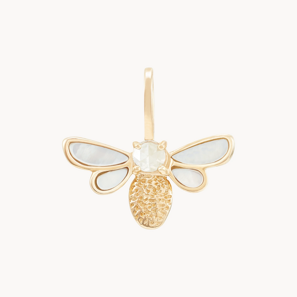 The Honey Glow Bee Charm by Bluboho is a gold pendant with intricate bee details. The wings feature a delicate mother of pearl inlay, creating a translucent white appearance. The bee's body boasts a textured 10k yellow gold finish, while the head is adorned with a small, clear gem. A loop allows for easy attachment to a chain.
