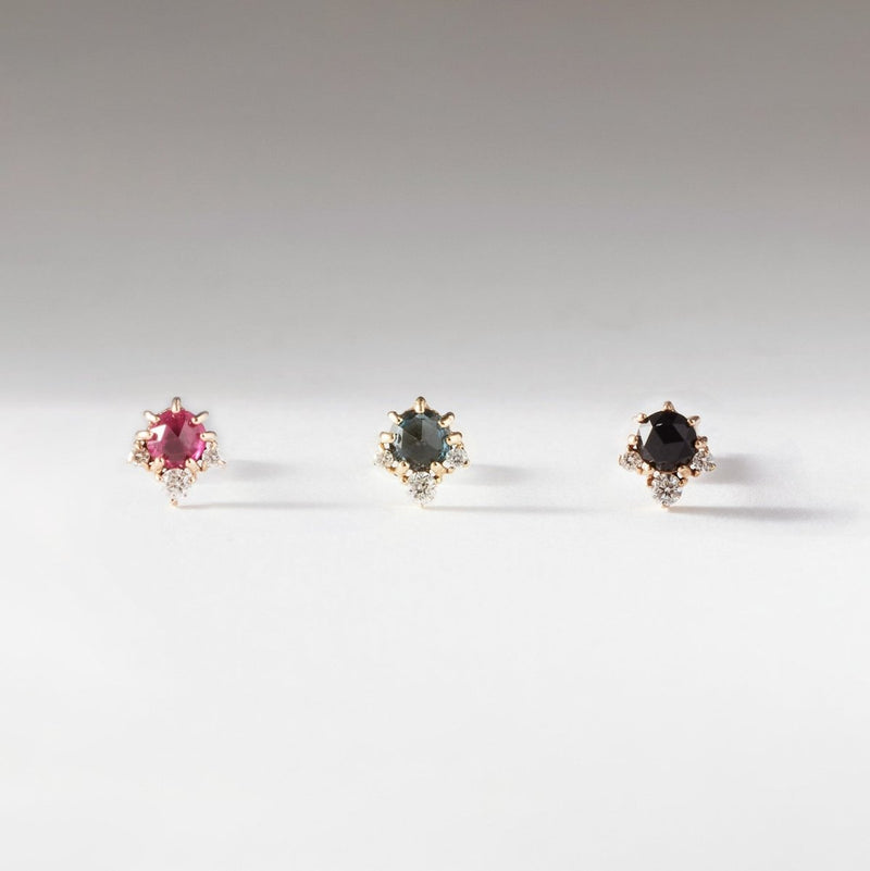 Three elegant rings with gold bands, each featuring a central gemstone and small diamonds. From left to right: a pink gemstone, a green gemstone, and the Full Moon Glow Diamond Black Onyx Earring - 14k yellow gold by bluboho. The rings are arranged in a row on a white surface with a soft gradient background.