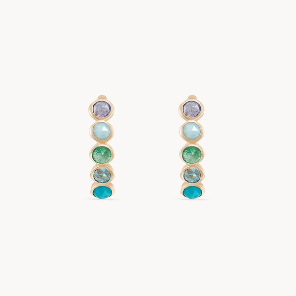 A pair of coastal nomad five stone mood hoops - 14k yellow gold, tanzanite, larimar, emerald, london blue topaz, turquoise by bluboho. The stones are arranged in gradient shades, ranging from purple at the top to pale blue, vivid green, and finishing with a bright turquoise at the bottom.