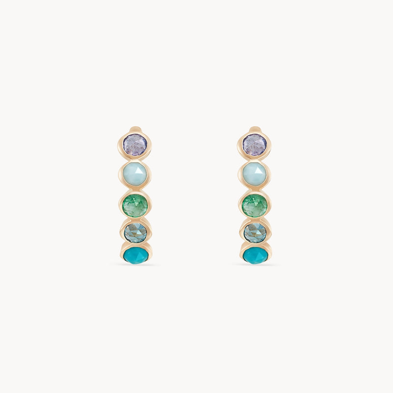 A pair of coastal nomad five stone mood hoops - 14k yellow gold, tanzanite, larimar, emerald, london blue topaz, turquoise by bluboho. The stones are arranged in gradient shades, ranging from purple at the top to pale blue, vivid green, and finishing with a bright turquoise at the bottom.