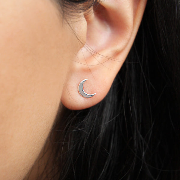 Close-up image of a person's ear adorned with the bluboho crescent moon earring in sterling silver. The silver-colored earring stands out against the person's dark hair, with the blurred background accentuating its elegance.