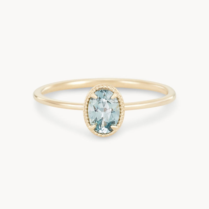 The Golden Glow One-of-a-Kind Ring by Beloved by Bluboho showcases a cyan green oval sapphire in a minimalist setting. The sapphire is accented with a fine beaded edge, highlighting its subtle hue. The ring features a thin, elegant 14k yellow gold band that perfectly complements the central gemstone.