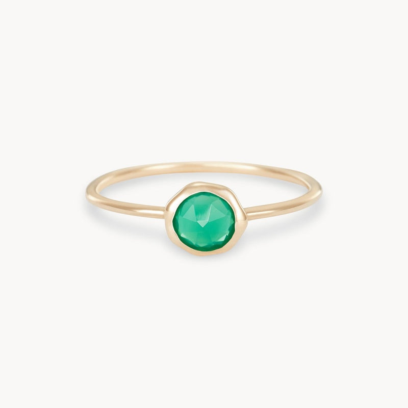 The green chalcedony mini mood ring, offered by bluboho, is a delicate piece crafted from 10k yellow gold. It features a small, round green chalcedony gemstone at its center. The stone is faceted to catch the light, adding a touch of elegance to the thin gold band. The ring design achieves a balance of simplicity and sophistication.