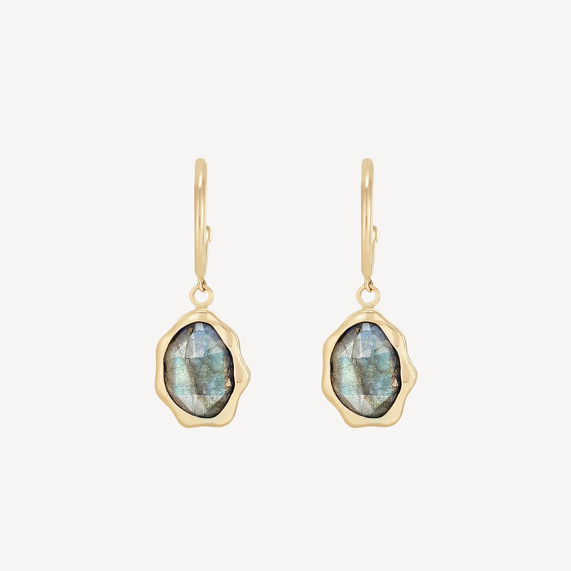 The labradorite mood hoop earrings by bluboho feature oval labradorite gemstones set in irregular, wavy 14k yellow gold frames. The simple, polished ear hooks complement the elegant design against a plain white background.