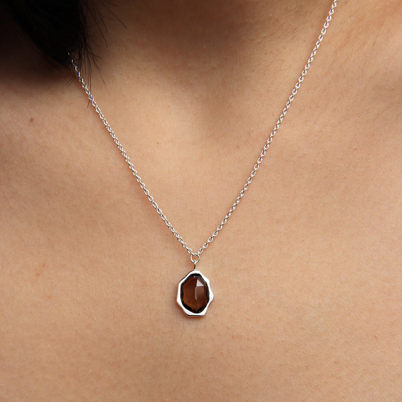 A close-up of a person's neck adorned with the sterling silver smoky quartz mood necklace by bluboho, featuring an octagon-shaped smoky quartz gemstone pendant. The background is the person's skin, and there are no other accessories or clothing visible.