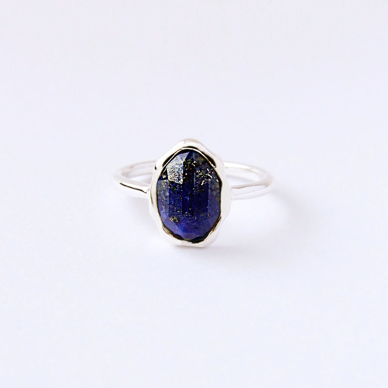 The lapis lazuli mood ring by bluboho showcases a large, faceted dark blue gemstone with metallic hints set in sterling silver. The plain white background emphasizes the gem's vibrant color and brilliance.