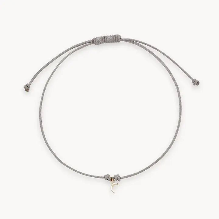 The Moon Phases Contemplation Cord Bracelet by bluboho features a minimalist gray string with an adjustable sliding knot closure and a delicate tiny crescent moon charm in 10k yellow gold. This bracelet is simple yet elegant, making it perfect for everyday wear.