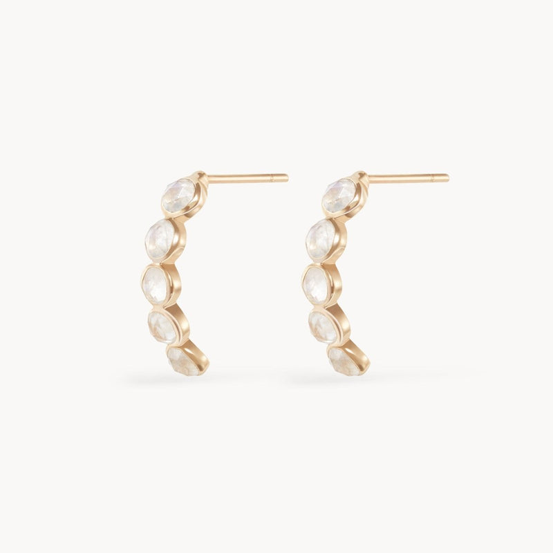 Introducing the "five stone moonstone mood hoop" by bluboho, a pair of exquisite 14k yellow gold earrings adorned with five round moonstones. Each gemstone is elegantly arranged in a graceful curve and set within individual round bezels, offering a delicate and sophisticated design. These stunning earrings feature post backs for secure fastening.