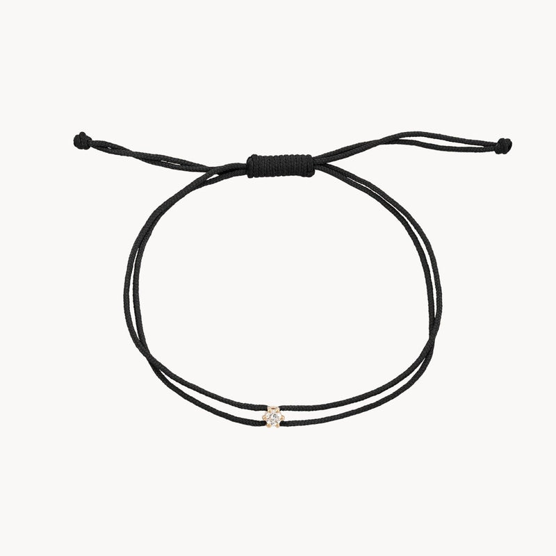 Introducing the Nova Diamond Black Cord Bracelet by bluboho, crafted from 10k yellow gold and black nylon. This minimalist bracelet features an adjustable sliding knot closure and a single clear diamond bead at its center, adding a subtle touch of elegance to its simple design. The background is plain white.