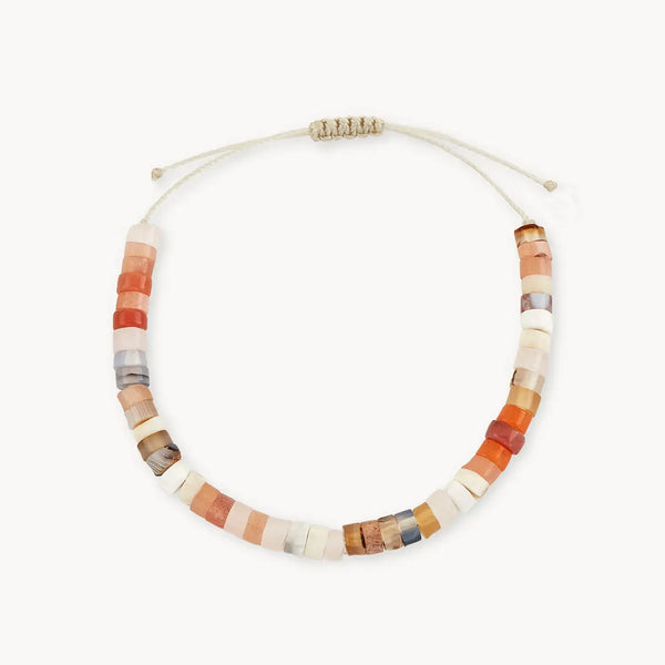 The bluboho sand dune bead bracelet features an array of colored round gemstone beads in shades of red, white, and beige. It has an adjustable beige cord with a knotted closure at the ends to allow for size adjustment.