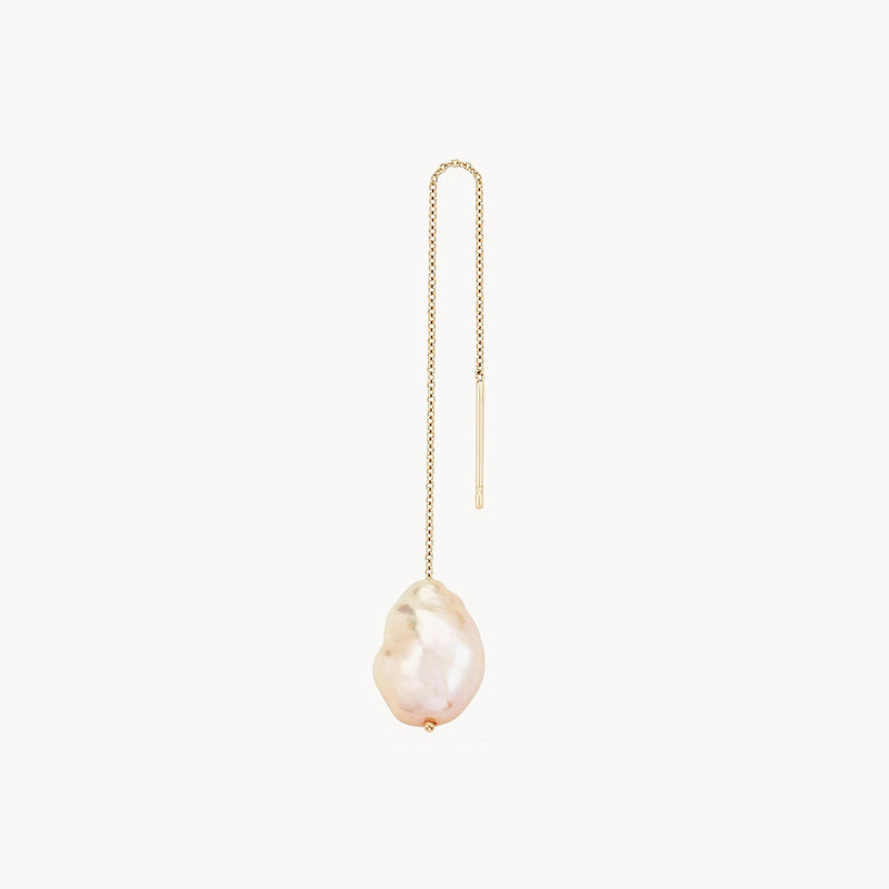 Close-up of a single sofia perla threader earring by bluboho, featuring a large, irregularly shaped white pearl at the end. The delicate 14k yellow gold chain threads directly through the ear, with one plain end and the other adorned with the elegant pearl. The background is white.