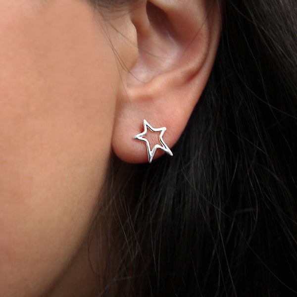 Close-up of an ear adorned with a bright star earring - sterling silver by bluboho. The background is slightly blurred, accentuating the earring and the ear. The hair is dark, and the skin tone is light.