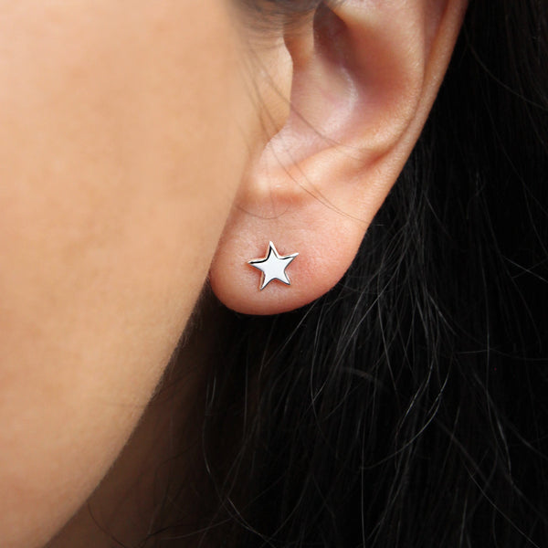 Close-up image of a person’s ear adorned with a small star-shaped bluboho stella earring in sterling silver. The earring is highlighted against the person's dark hair, with the background out of focus to emphasize the bluboho stella earrings silver.