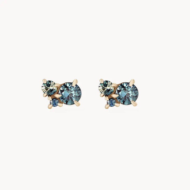 A pair of stud earrings featuring clusters of small, round gemstones in varying shades of blue and green, each set in a gold prong setting. The something blue tie dye moonchild ombre sapphire earring - 14k yellow gold, blue sapphire by bluboho are displayed on a plain white background.