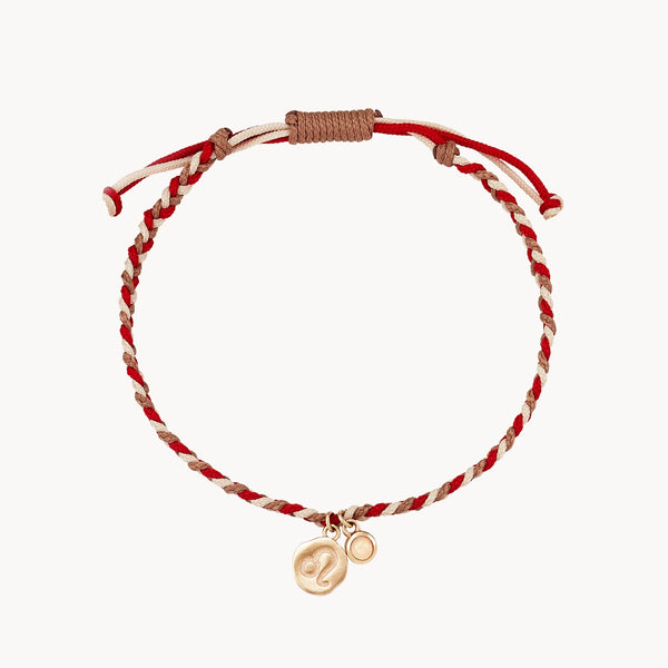 A thin, adjustable bracelet with twisted red and beige cords. It has a small, round gold charm hanging from it, featuring an engraved symbol resembling the letter 'P'. The ends of the bracelet are finished with knots. This is the leo zodiac bracelet fire element cord bracelet - 10k yellow gold, opal, cord from bluboho.