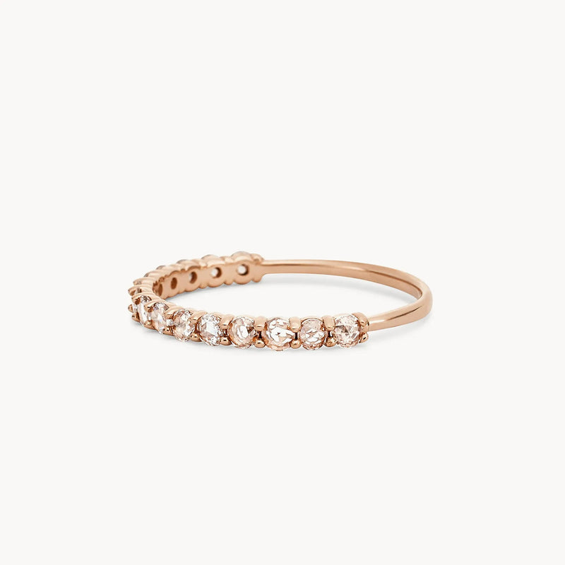 The Moonglade ring by beloved by bluboho, crafted in 14k rose gold, features a row of sparkling white diamonds set in prongs that gradually taper towards the sides. This delicate piece showcases an elegant and minimalist design with a slightly curved band, enhancing its sophisticated appearance.