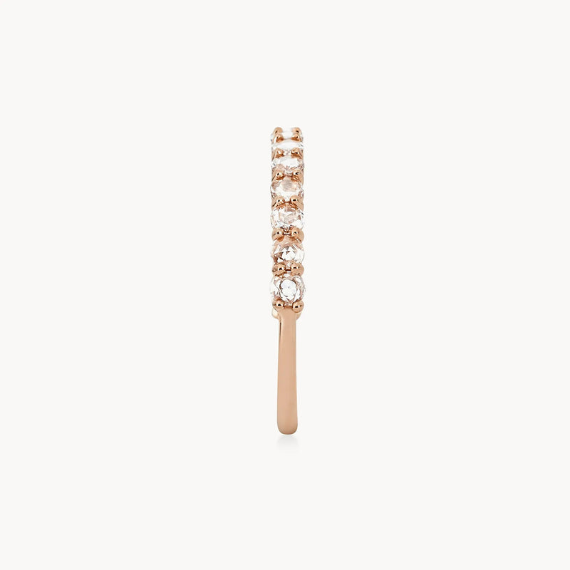 The Moonglade ring by beloved by bluboho showcases a stunning row of small, round white diamonds set along the top half of its 14k rose gold band. The slender band features a polished finish, and the side-view image highlights the intricate diamond settings against a plain white background.