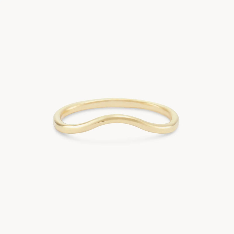 The plain wave band by beloved by bluboho is a 14k yellow gold ring featuring a subtle, wavy design in the center that forms a gentle curve. It boasts a smooth and polished finish against a plain white background.