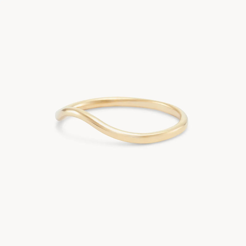 The "plain wave band - 14k yellow gold" by Beloved by Bluboho is a delicate ring featuring a minimalist wave design with a subtle, smooth curve along its thin band. It boasts a polished finish and is visually set against a plain white background.