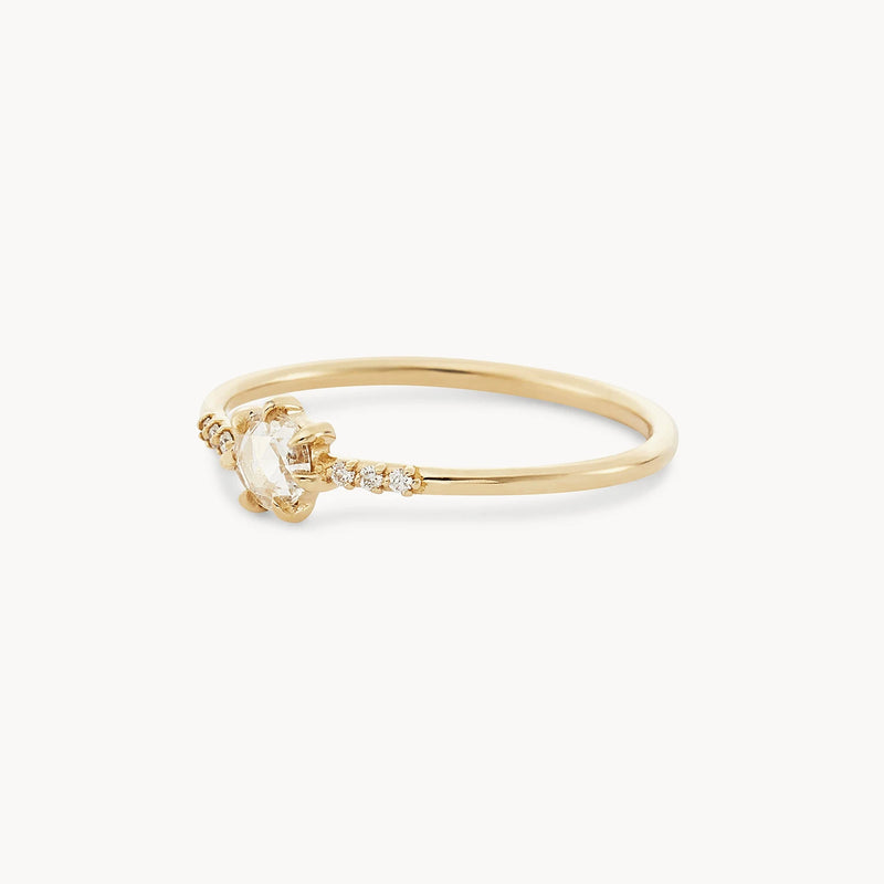 The supernova ring by bluboho features a pear-shaped white diamond flanked by small round diamonds on a thin, smooth 14k yellow gold band. This delicate piece boasts a minimalist design with a modern yet elegant appearance.