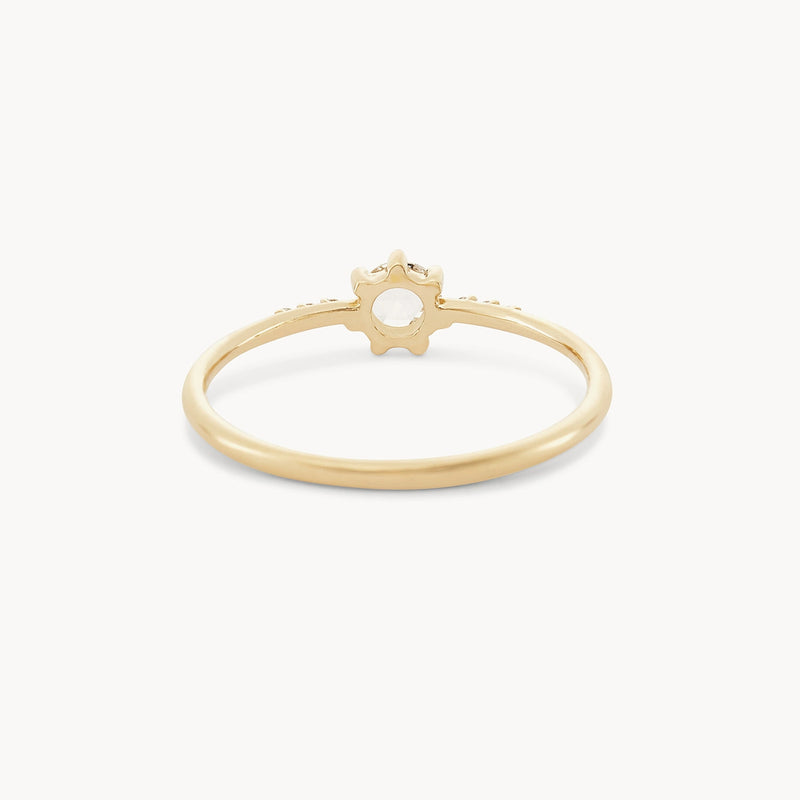 The Supernova Ring by Bluboho features a minimalist and elegant design, with a slender 14k yellow gold band and a small, flower-shaped setting at its center that encloses a tiny round white diamond. This delicate piece makes for an exquisite yet subtle statement accessory, displayed against a plain white background.