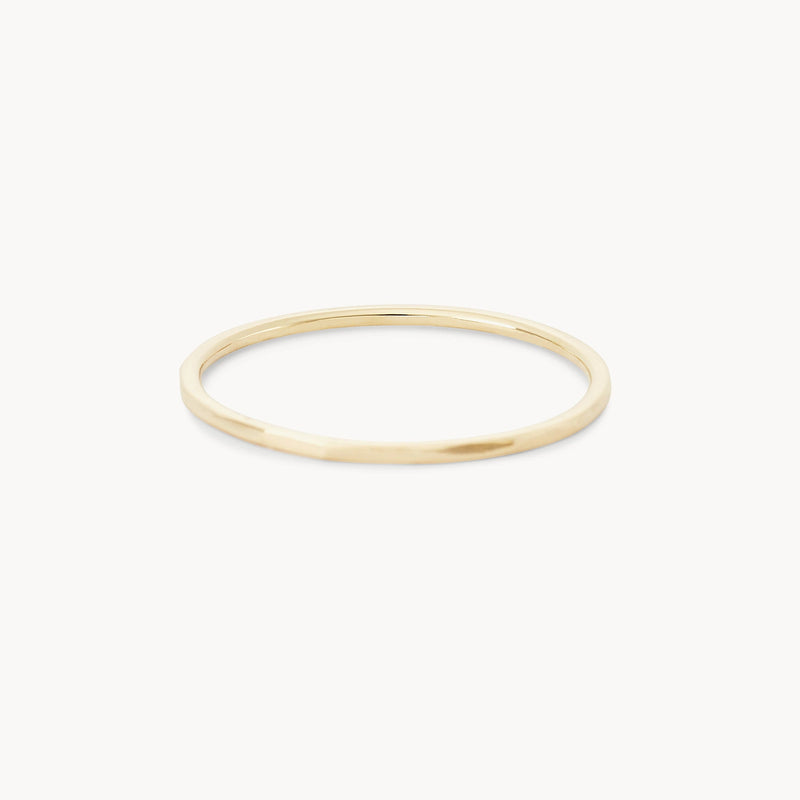 A minimalist, thin "Faceted Felicity Stacking Ring" by bluboho is pictured against a plain white background. The 10k yellow gold ring has a sleek and simple design, featuring a smooth, round band that signifies elegance and subtlety.