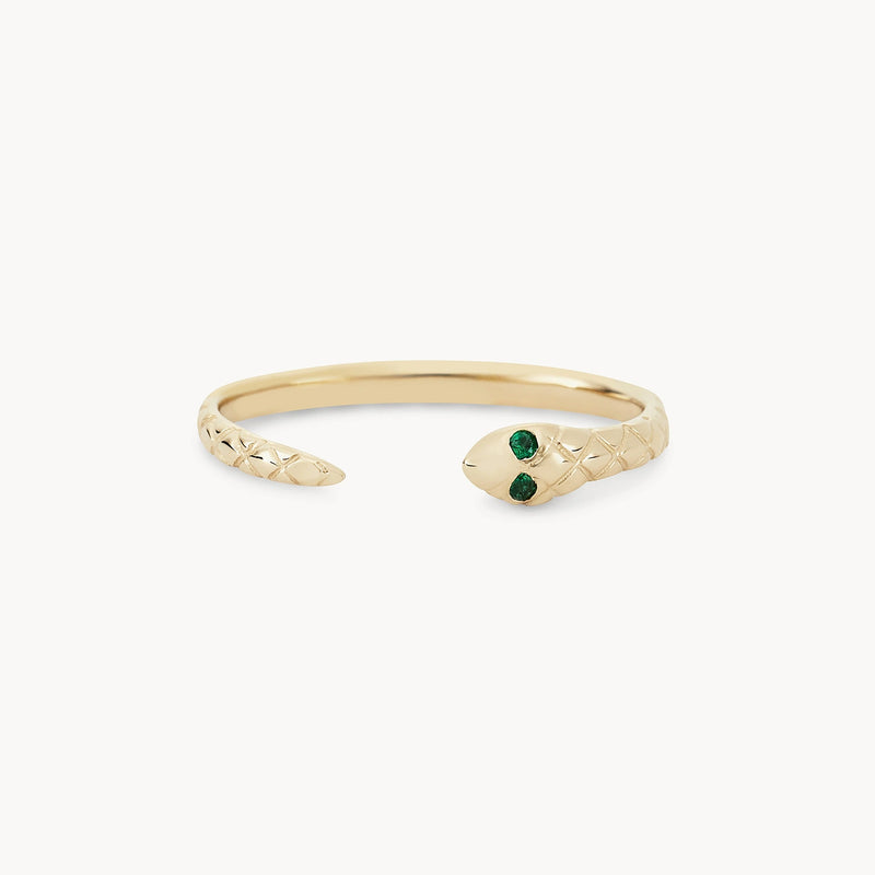 The revival emerald snake ring by bluboho is crafted in 14k yellow gold, featuring an intricate serpentine design with detailed scales. It showcases two green gemstones set as the eyes of the snake. The ring is open-ended, with the snake's head and tail forming the clasp.