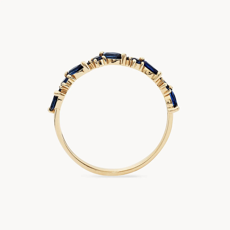 Introducing the Reverie Band by Beloved by Bluboho: A 14K yellow gold ring adorned with a series of small, rectangular blue sapphires set along the top half. The sapphires are arranged in a slightly jagged design, each securely held by gold prongs against a plain white background.