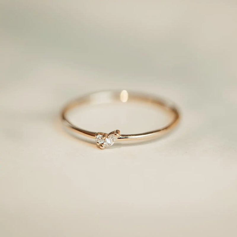 A delicate Lean on me ring - 14k yellow gold, white diamond by bluboho with a small, round, clear gemstone in the center rests on a light, soft-focus background. The simple design emphasizes elegance and minimalism.