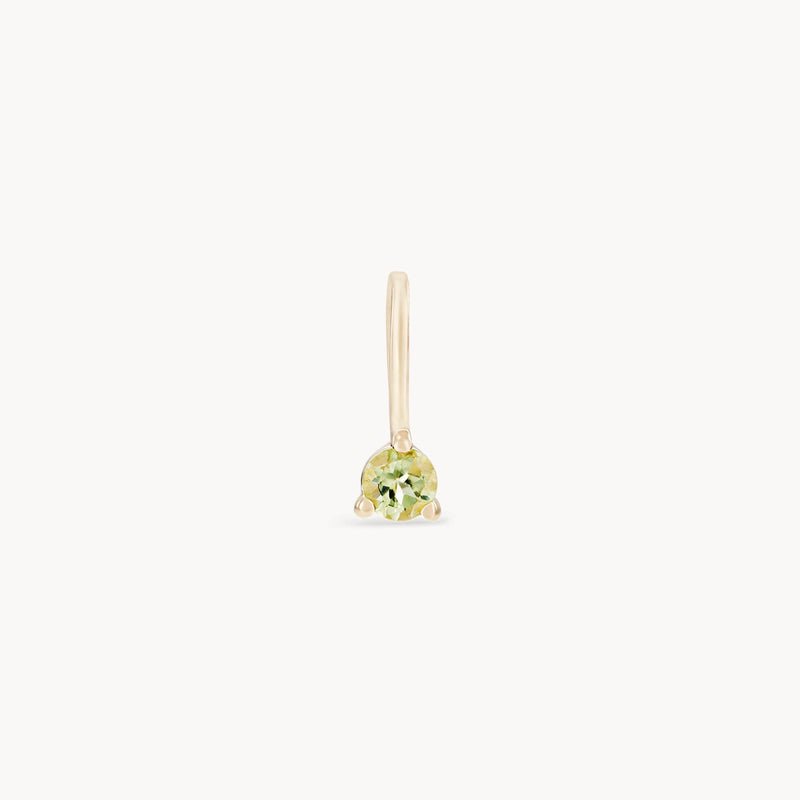 The serendipity august birthstone charm by bluboho is a single 10k yellow gold earring, showcasing a delicate, round-cut peridot gemstone. Its minimalistic design features a smooth gold hook above the gemstone, allowing it to dangle gracefully. The white background highlights the charm's simplicity and elegance.