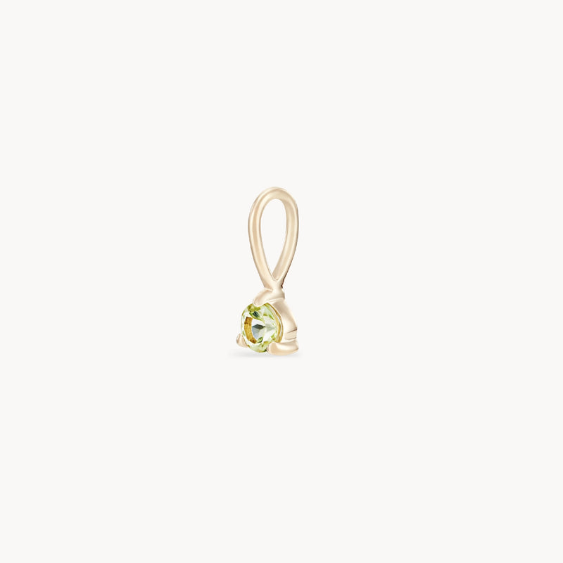 A close-up image of the serendipity august birthstone charm by bluboho, crafted from 10k yellow gold and featuring a small, round peridot gemstone. The charm boasts a simple, elegant design with a loop at the top for attaching to a necklace. The peridot is securely held in place by a prong setting.