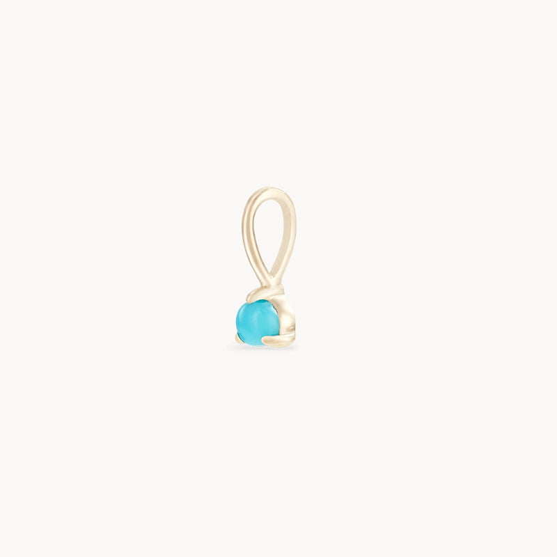 The Serendipity December Birthstone Charm by Bluboho showcases a single, small turquoise stone in a delicate 10k yellow gold setting. The minimalist and elegant design accentuates the vibrant blue of the stone against the shiny gold frame, all presented against a plain white background.