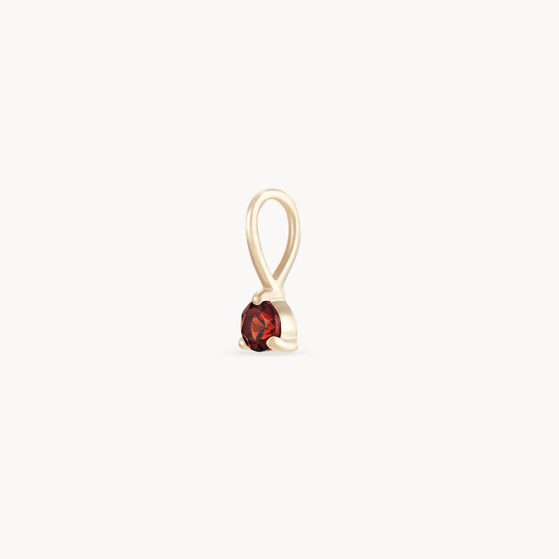 Presenting the "serendipity january birthstone charm" by bluboho - a 10k yellow gold charm featuring a single round garnet gemstone. The minimalist design includes a loop at the top for easy attachment to a necklace, and the garnet is securely held in a prong setting against a plain white background.