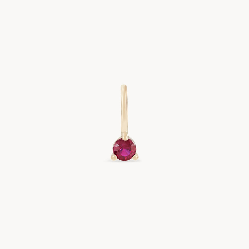 The bluboho Serendipity July Birthstone Charm is a delicate 10k yellow gold earring that showcases a single round ruby, elegantly set in a prong setting. The simple hook design makes it easy to wear, and the prominently displayed gemstone highlights its vibrant color against the minimalist gold setting.