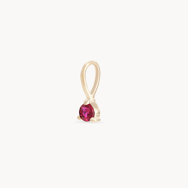 A delicate gold pendant from bluboho, known as the serendipity july birthstone charm, crafted in 10k yellow gold with a single loop at the top. It features a small round-cut ruby securely held in a minimalist setting, against a plain white background.