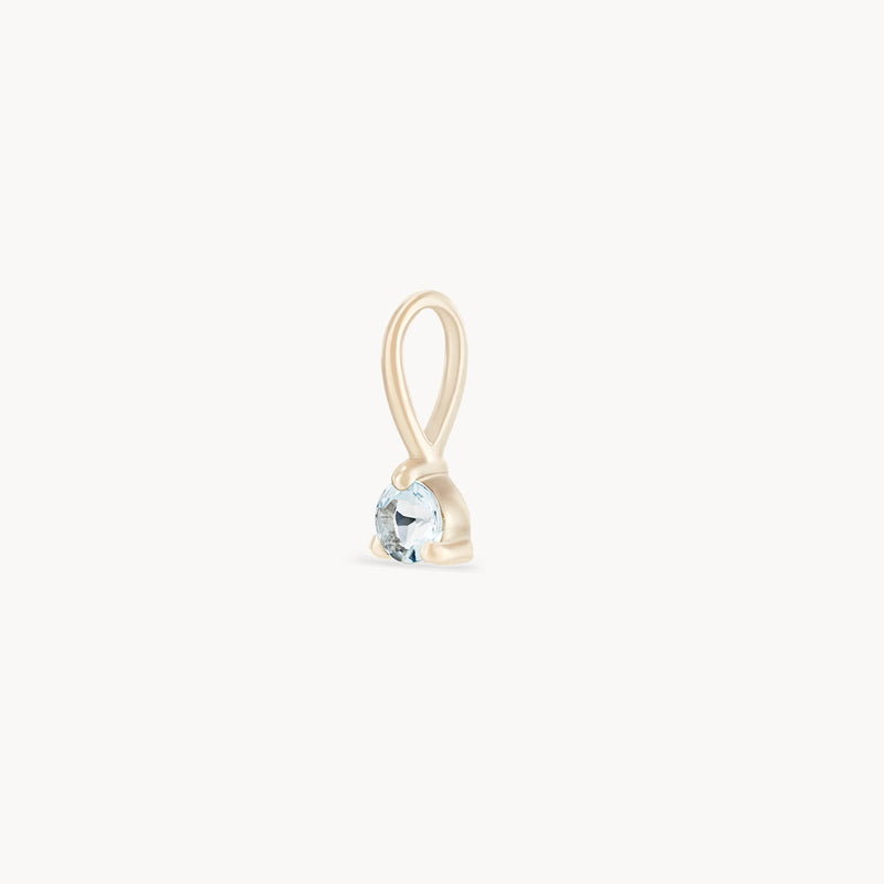 The bluboho Serendipity March Birthstone Charm showcases a single, round-cut aquamarine gemstone suspended within a simple 10k yellow gold loop. The design is minimalistic, emphasizing the gemstone as the focal point, set in a small gold prong setting against a plain white background.