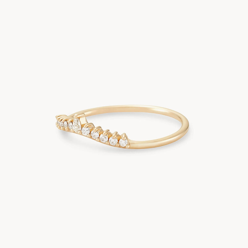 The Sunbeam Ring by Beloved by Bluboho showcases a delicate design in 14k yellow gold, featuring a row of small, sparkling white diamonds arranged in an elegant asymmetrical curve that extends on one side of the band. The minimalistic design ensures the diamonds are securely set in prongs, all against a pristine white background.