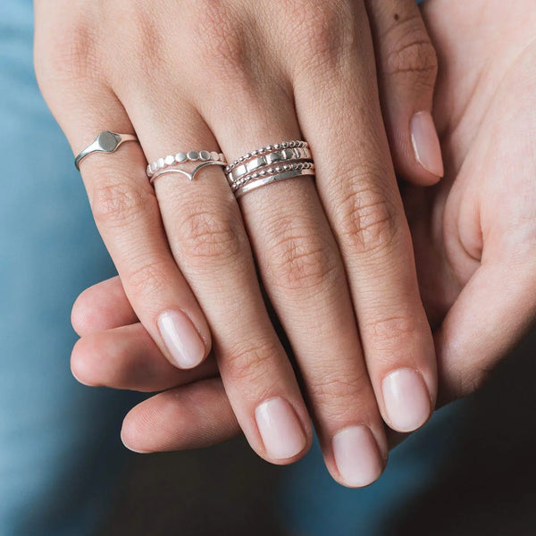 Close-up of a person's hand showcasing four rings on two fingers. One is the "Abacus ring - sterling silver" by bluboho, featuring three connected thin bands with small beads. The other rings include one with a simple band design, another with a half-moon shape and dots, and a third featuring a chain-like pattern.