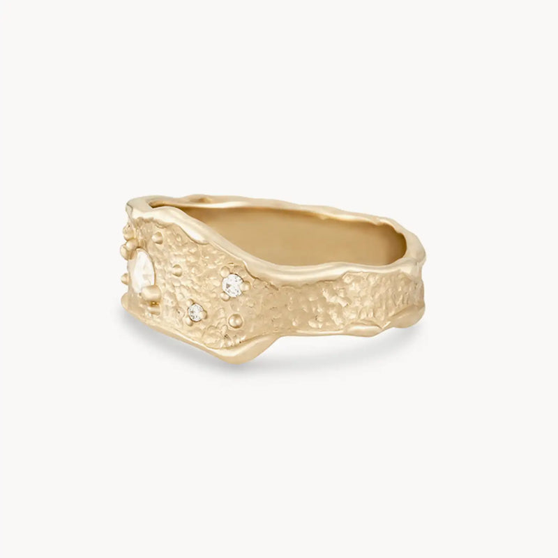 The Luminous Honey Diamond Ring from bluboho, crafted in 14k yellow gold and adorned with white diamonds, features a chunky design with a textured, uneven surface. The band has a wavy, irregular edge that gives it an organic, handcrafted appearance. Its matte finish enhances the ring's rustic and unique design.