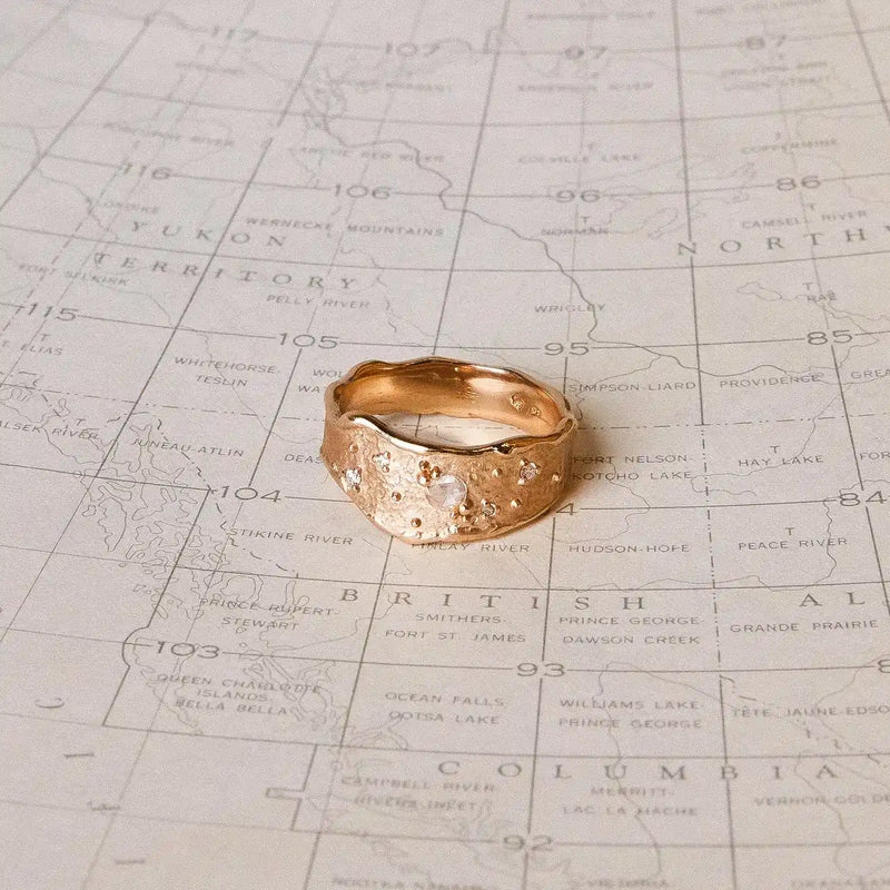 A Luminous Honey Diamond Ring from bluboho, crafted in 14k yellow gold and adorned with white diamonds, is placed on a vintage map. The map shows details of the Yukon, British Columbia, and some parts of Alaska, with various geographic regions and locations labeled.