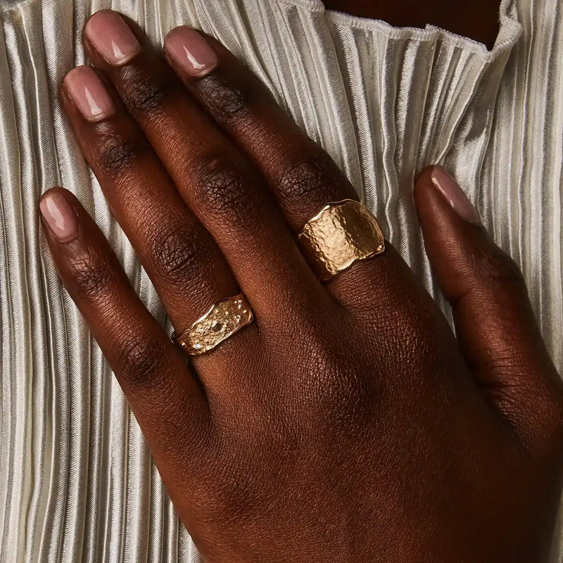 Close-up of a person's hand with neatly manicured nails, wearing the stunning Luminous Honey Diamond Ring in 14k yellow gold with white diamonds from bluboho on their middle finger. The hand rests on a pleated white fabric, providing a contrast to the skin tone and highlighting the beauty of the jewelry.