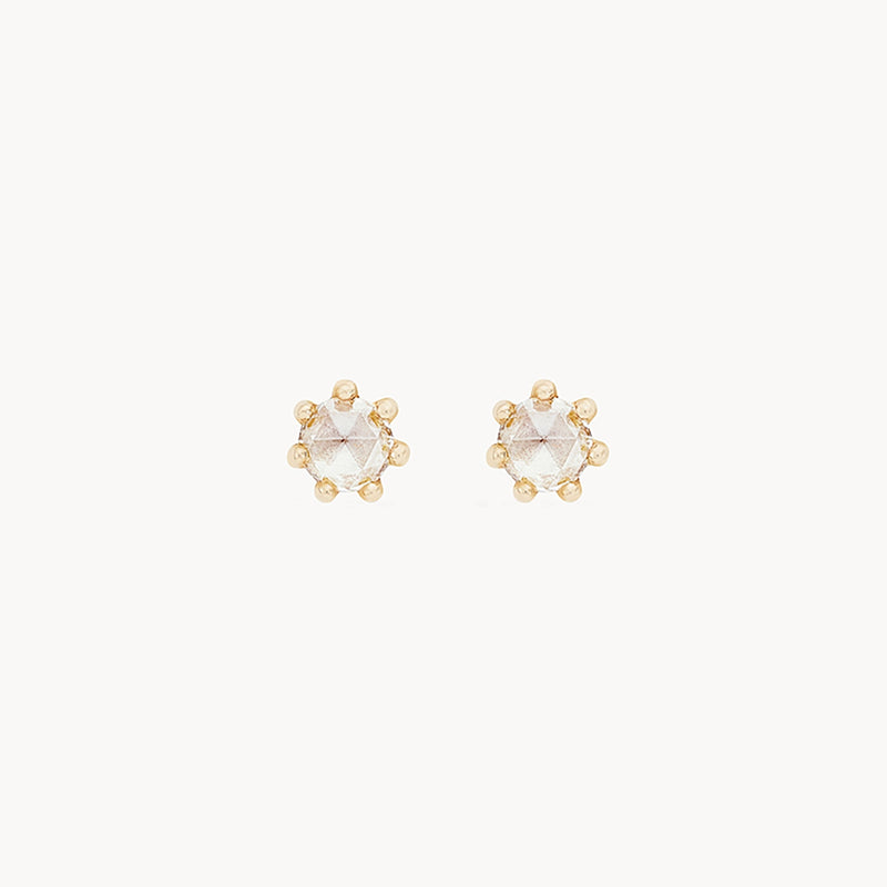 A pair of delicate nova earring - 14k yellow gold, white diamond by bluboho featuring a central clear gemstone surrounded by a hexagonal arrangement of six smaller golden beads, set against a white background.