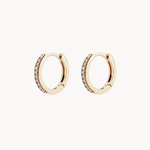 The bluboho shine on hoop earring - 14k yellow gold, white diamond encrusted with small, sparkly diamonds along the front outer edge. The earrings have a smooth and polished finish, showcasing a luxurious and elegant design against a plain white background.