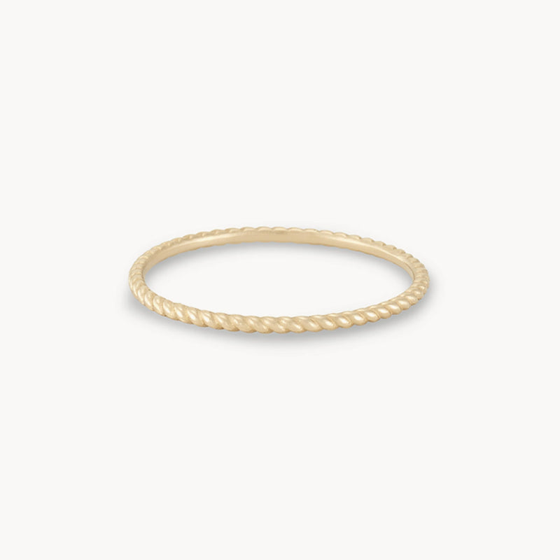 A thin, gold twisted rope-style ring is displayed against a white background. The bluboho twisted stacking ring - 10k yellow gold features a delicate, minimalist design with a textured surface resembling a twisted rope.