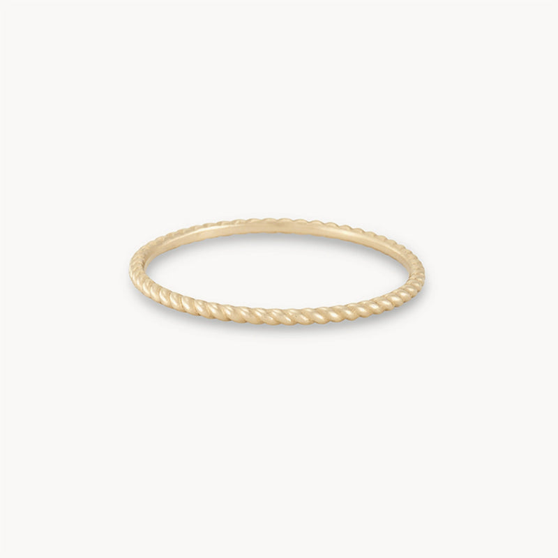 A thin, elegant twisted stacking ring - 10k yellow gold by bluboho with a twisted rope design is displayed against a plain white background. The ring is circular and delicately crafted, showcasing fine detailing that resembles a rope texture.