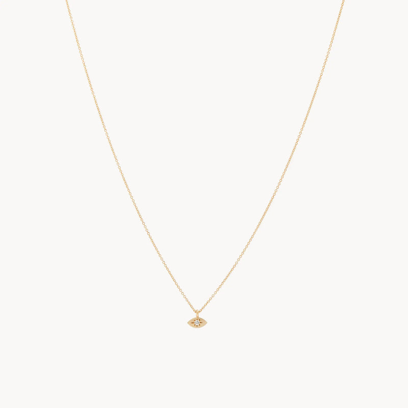 A delicate visionary evil eye pendant from bluboho, crafted in 14k yellow gold with a small, eye-shaped design featuring a single tiny crystal at its center, set against a white background.
