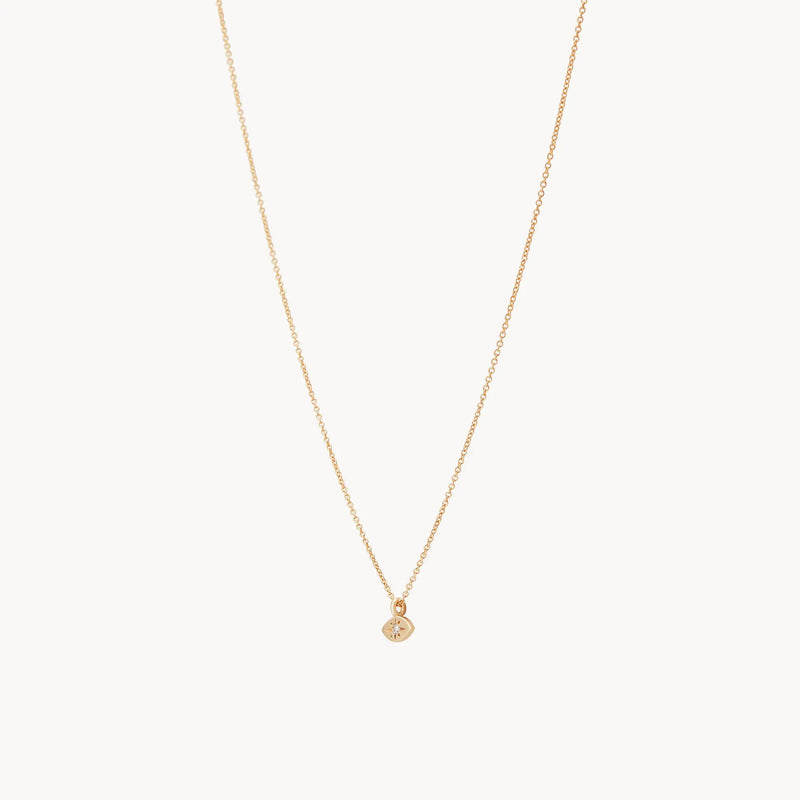 The visionary evil eye pendant by bluboho features a thin 14k yellow gold chain and a small round charm adorned with a tiny central gemstone, elegantly displayed against a plain white background.