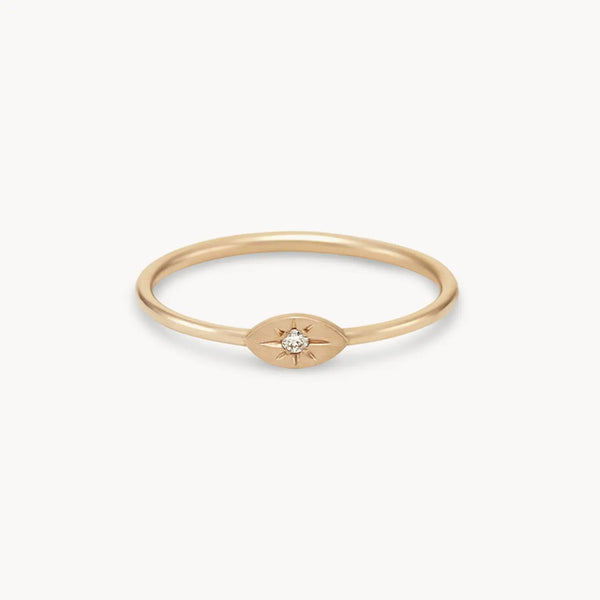 The visionary evil eye ring by bluboho is a thin, 14k yellow gold ring featuring a brilliant diamond set in an oval-shaped, starburst design on a plain background.